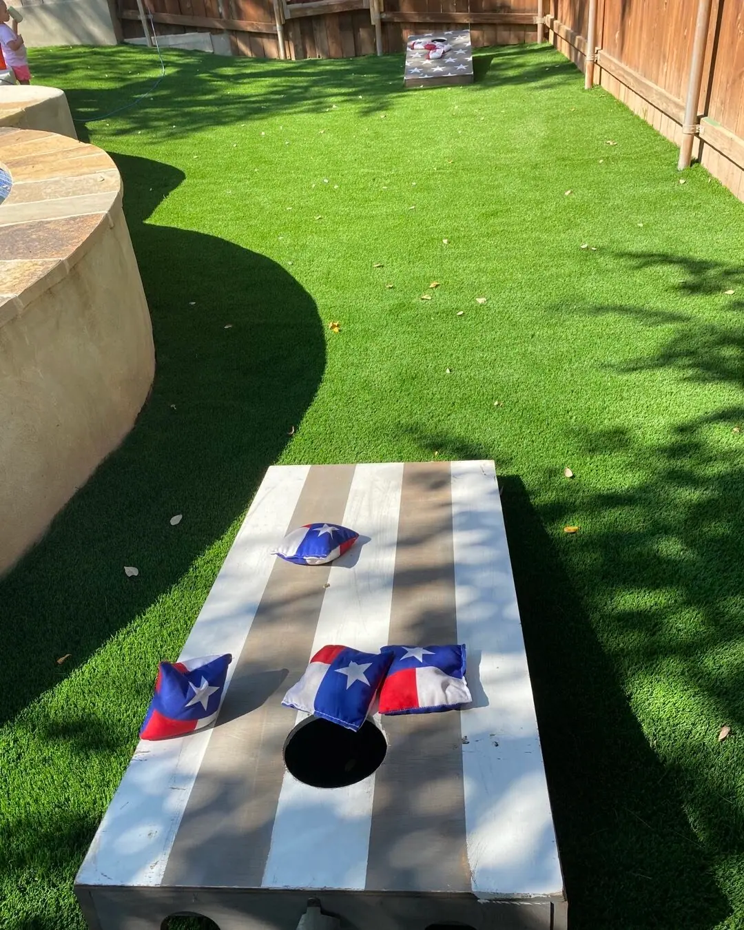 Cornhole board on artificial turf in a fenced yard